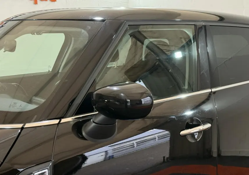 Vue rapprochée du côté gauche d'une MINI Countryman noire 2020, mettant en valeur la portière et le rétroviseur noir brillant.