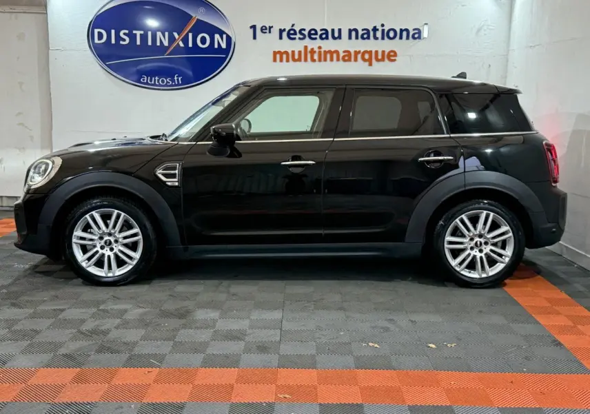 Profil côté gauche d'une MINI COUNTRYMAN Cooper D Business Design noire, vue en intérieur sur sol gris et orange.