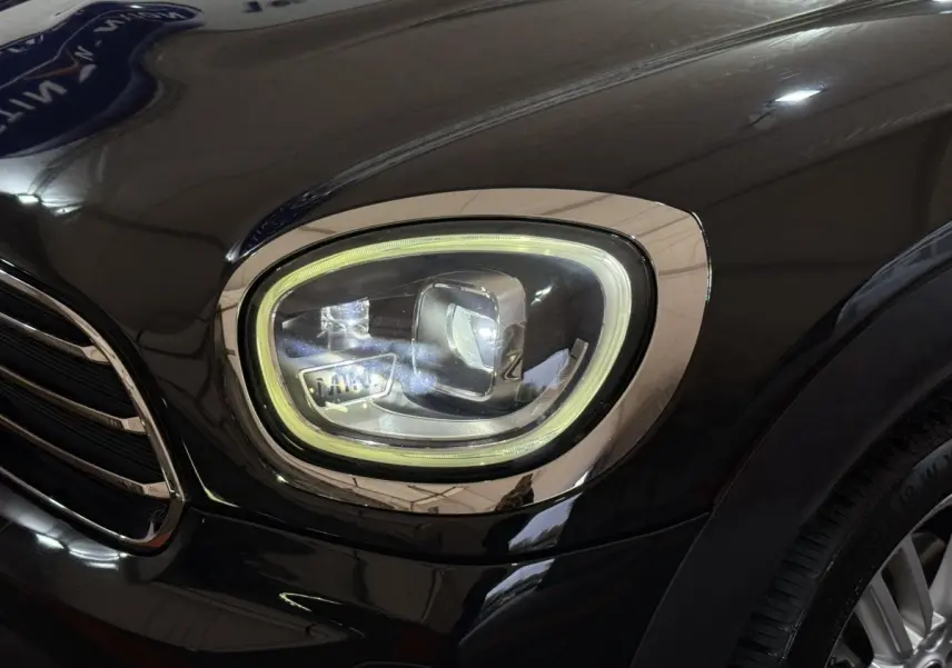 Gros plan sur le phare avant droit LED d'une MINI Countryman noire, soulignant son design moderne et ses finitions chromées.