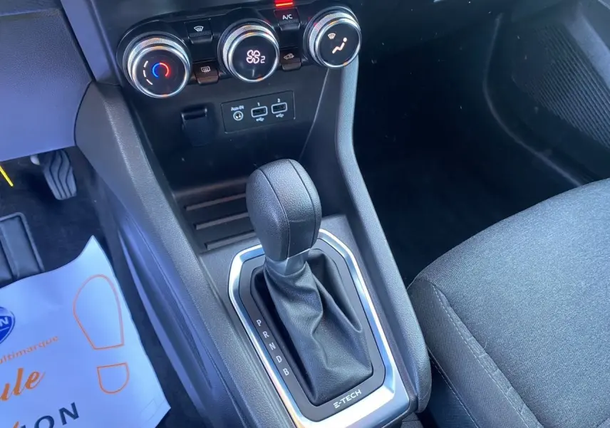 Gros plan sur la console centrale noire de la Renault Clio V E-Tech 140 avec levier de boîte auto et commandes de climatisation.