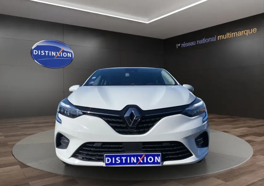 Vue avant d'une Renault Clio V blanche, avec calandre noire et logo Renault centré, en showroom Distinxion.