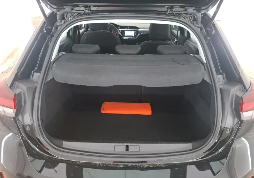 Coffre ouvert vu de l'arrière d'une Opel Corsa Noir Perla 2023, avec cache-bagages et un objet orange à l'intérieur.