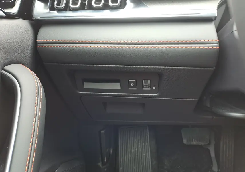 Détail intérieur côté gauche du tableau de bord noir avec surpiqûres rouges et commandes près des pédales du BYD SEAL U 2025.