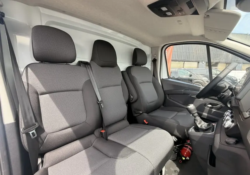Vue intérieure côté conducteur du Renault Trafic Fourgon 2025 avec sièges tissu gris et tableau de bord noir.