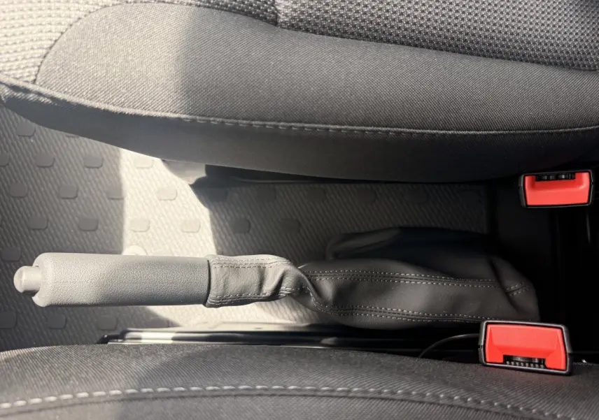 Vue rapprochée de la poignée de frein à main en cuir noir entre les sièges avant gris foncé du Renault Trafic Fourgon blanc.