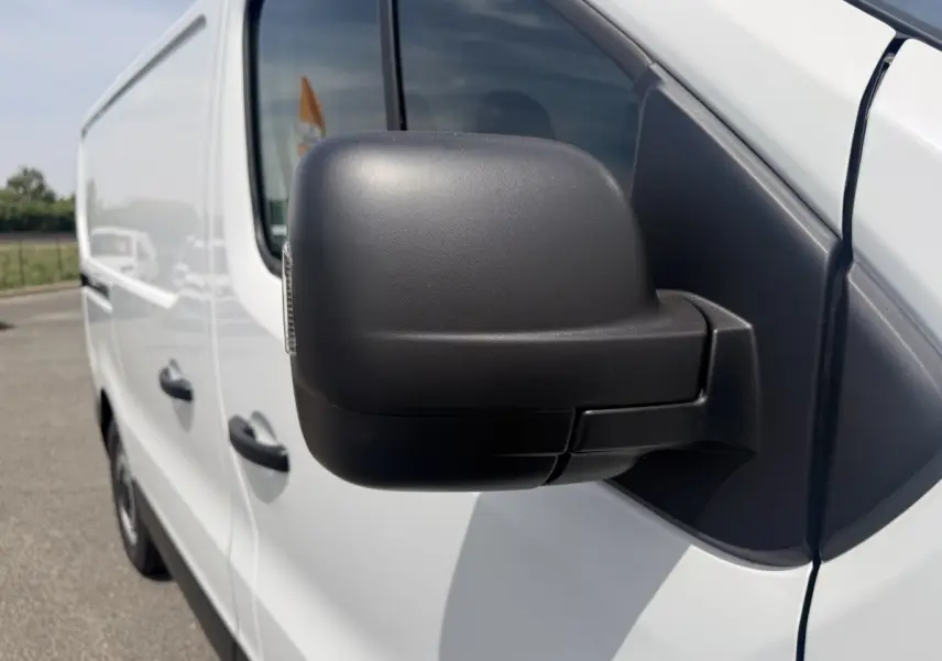 Rétroviseur noir en gros plan sur le côté gauche d’un Renault Trafic Fourgon blanc, vue avant latérale.