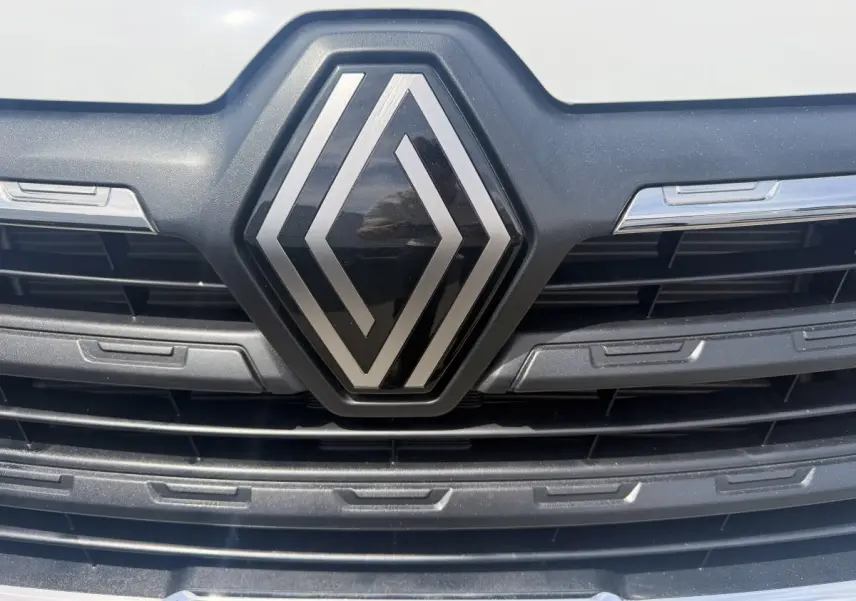 Gros plan sur la calandre noire avec le logo Renault argenté du Trafic Fourgon blanc, vue frontale rapprochée.