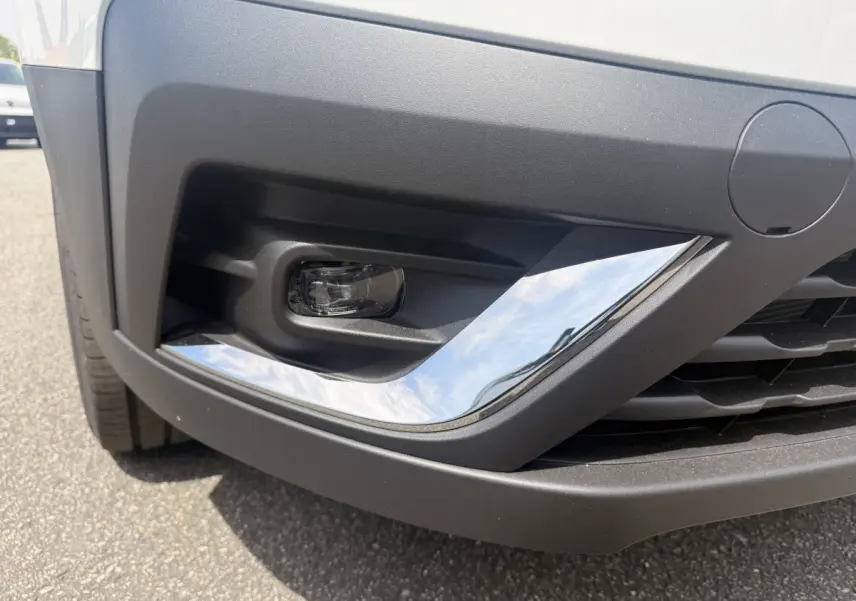 Gros plan sur le pare-chocs avant droit blanc du Renault Trafic Fourgon avec antibrouillard et insert chromé.