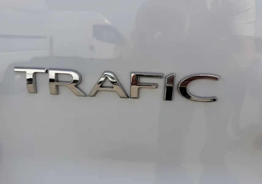 Gros plan sur l’inscription chromée TRAFIC sur la porte arrière d’un fourgon Renault Trafic blanc.
