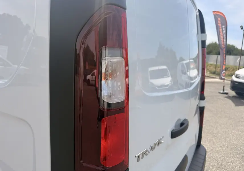 Vue arrière droite du Renault Trafic Fourgon blanc avec feu arrière vertical et logo TRAFIC visible.