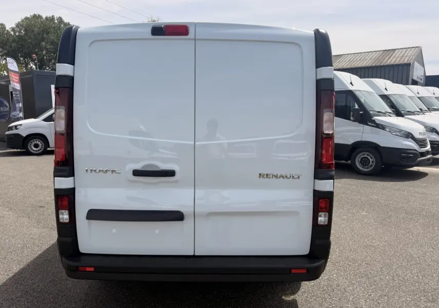 Vue arrière d'un Renault Trafic Fourgon blanc avec portes battantes et feux verticaux rouges.