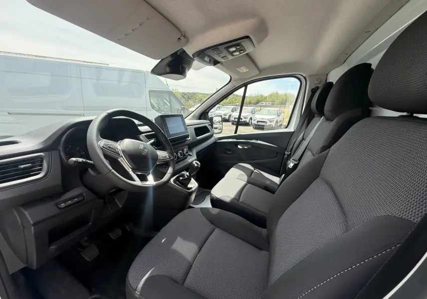 Vue intérieure avant droite du Renault Trafic Fourgon 2025, montrant les sièges noirs et le tableau de bord avec écran tactile.