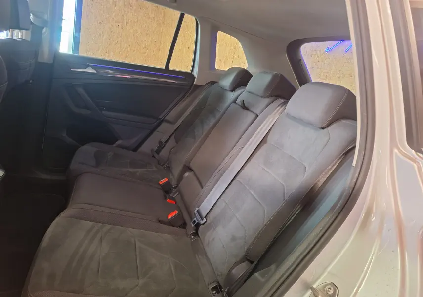 Vue intérieure des sièges arrière en Microfleece gris du Volkswagen Tiguan 2021, avec ceinture de sécurité et éclairage d'ambiance bleu.