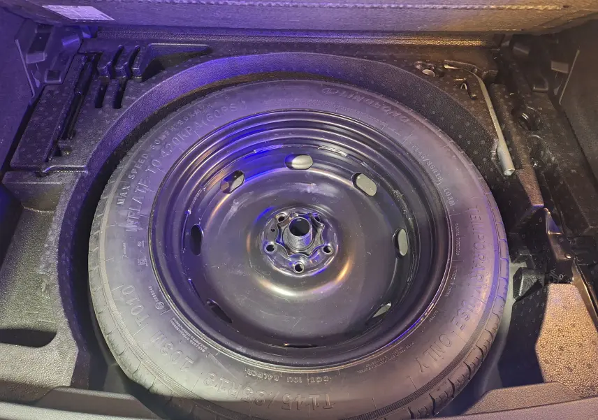 Gros plan sur la roue de secours noire dans le coffre du Volkswagen Tiguan gris, avec outils de changement rangés autour.