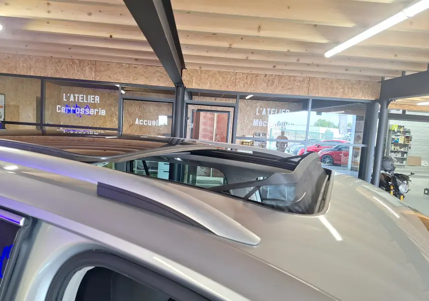 Toit ouvrant panoramique ouvert sur un Volkswagen Tiguan gris, vue rapprochée du toit et des barres de pavillon côté gauche.