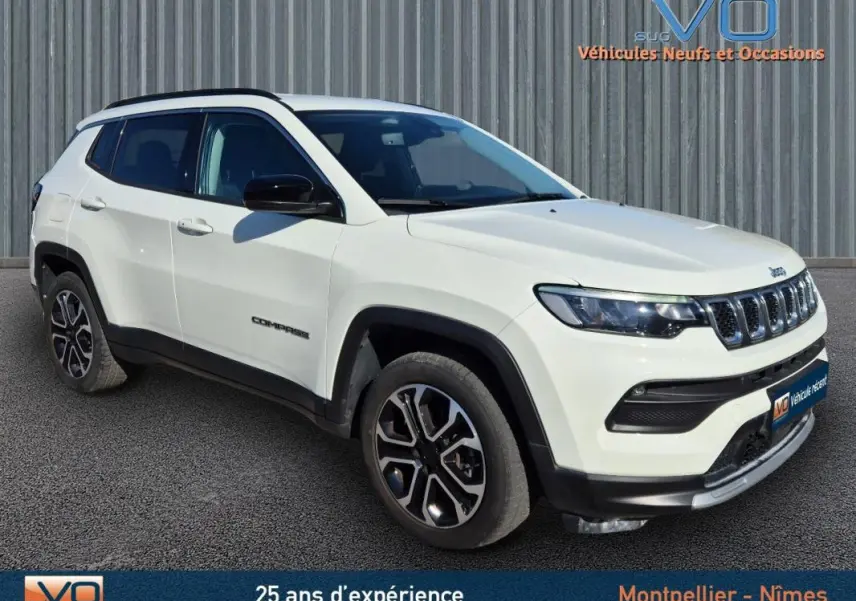 Jeep Compass blanc vue 3/4 avant droit avec jantes 18 pouces et barres de toit noires sur fond urbain.