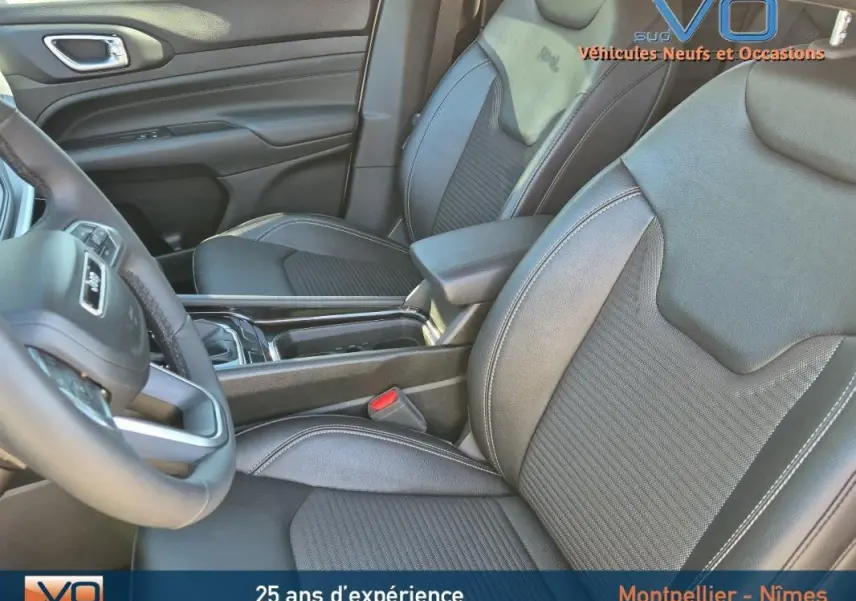 Vue intérieure sur les sièges avant noirs en cuir du Jeep Compass 2023 avec accoudoir central et volant partiel visible.