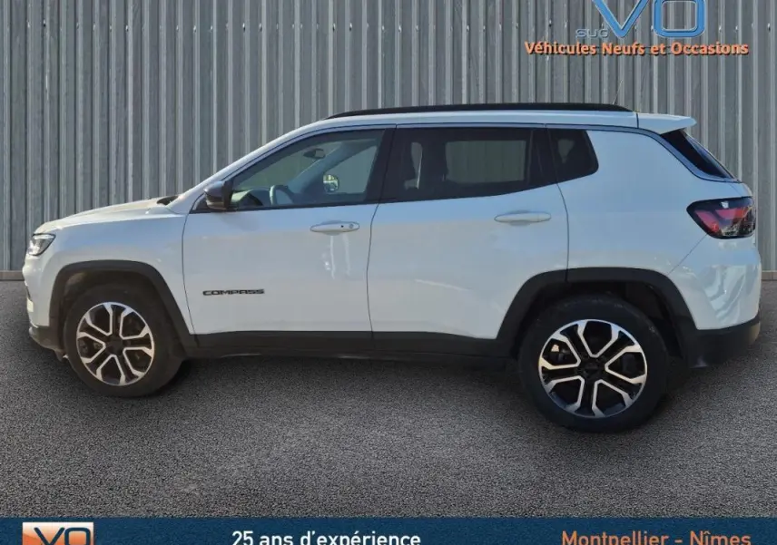 Vue de profil côté gauche d'un Jeep Compass blanc 2023 avec jantes 18 pouces et barres de toit noires.
