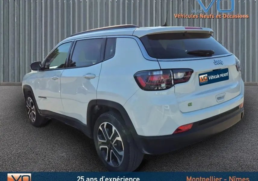 Vue 3/4 arrière gauche d'un Jeep Compass blanc 2023 avec barres de toit et jantes 18 pouces.