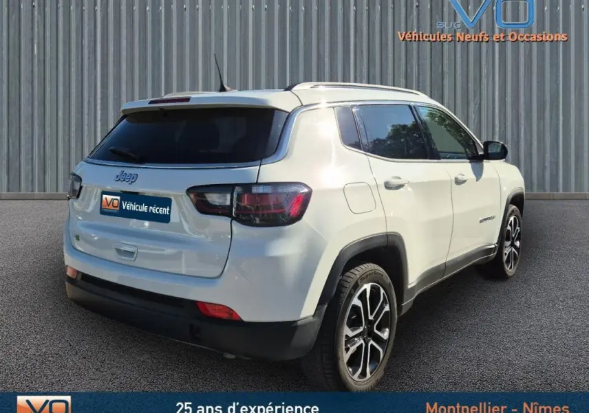 Vue 3/4 arrière droite d'un Jeep Compass blanc 2023 avec barres de toit et jantes 18 pouces visibles.
