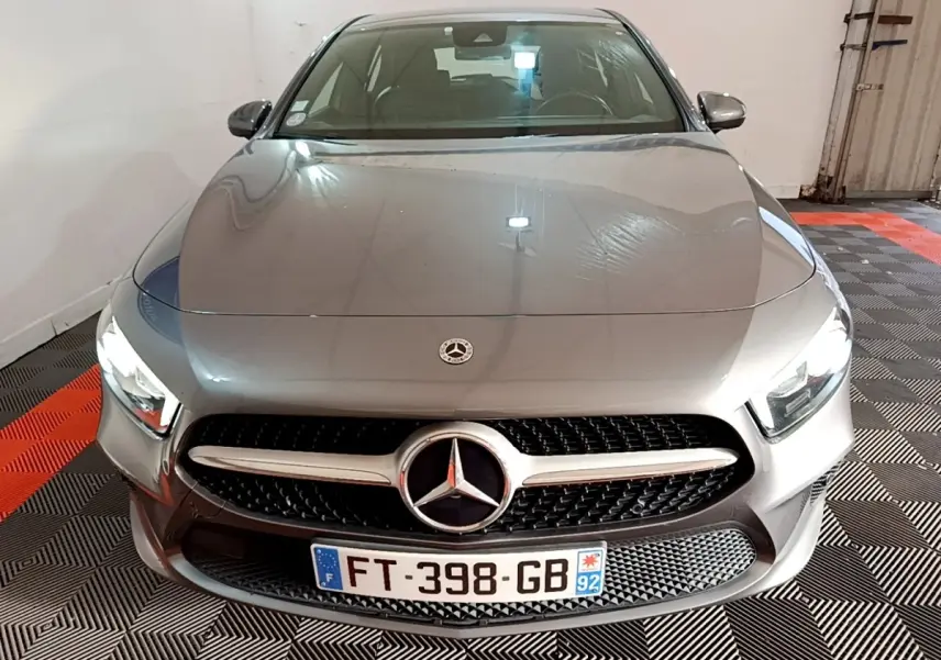 Vue avant d'une Mercedes Classe A gris foncé avec calandre étoilée et phares LED allumés dans un garage.
