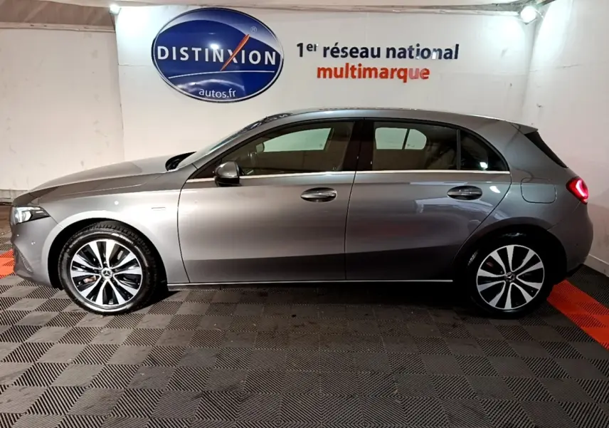 Profil côté gauche d'une Mercedes Classe A 250 e Business Line gris foncé avec jantes alliage et feux arrière allumés.