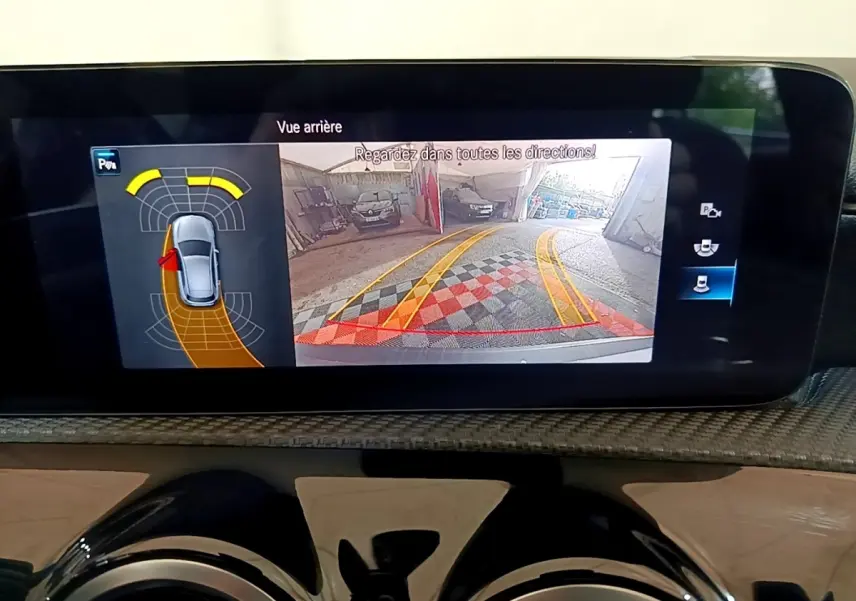 Écran multimédia affichant la caméra de recul et l'aide au stationnement du Mercedes Classe A gris foncé en intérieur.