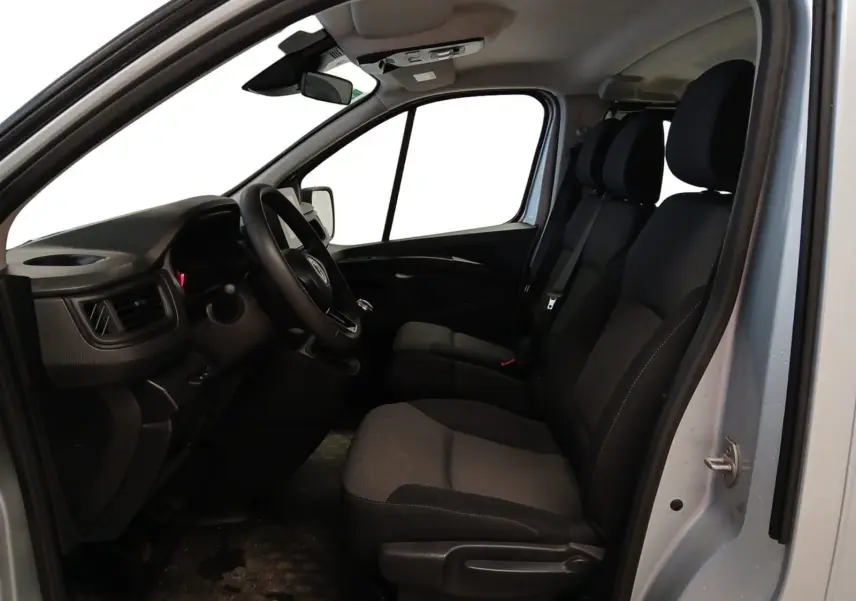 Vue intérieure côté conducteur du Renault Trafic Combi gris clair métal 2023, montrant les sièges avant et le tableau de bord.