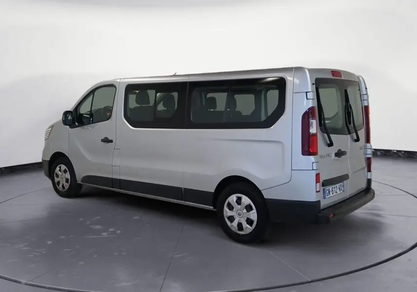 Vue 3/4 arrière droite d’un Renault Trafic Combi gris clair métal, montrant ses grandes fenêtres latérales et ses portes arrière vitrées.