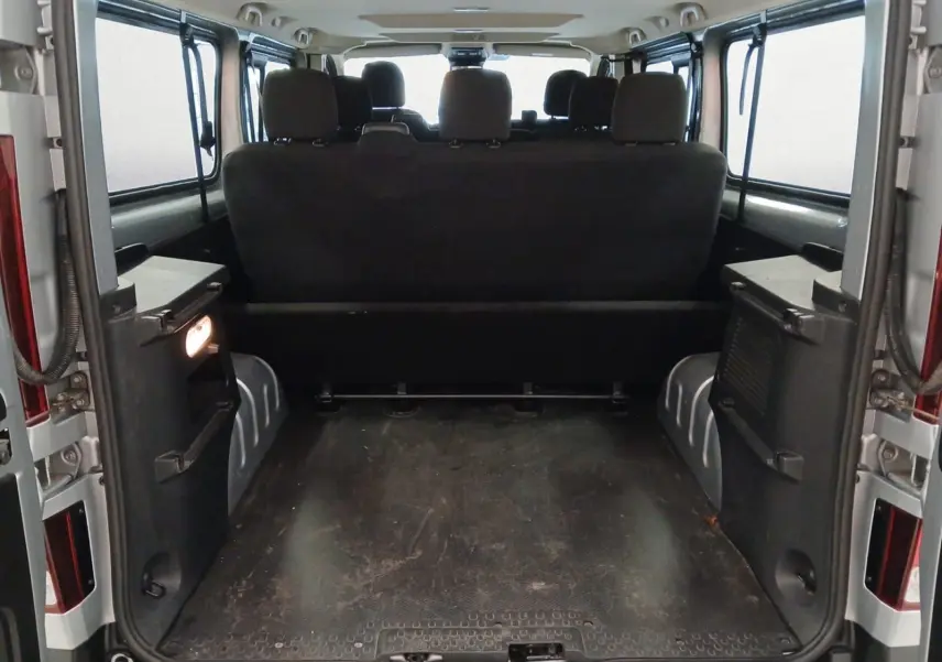 Vue arrière ouverte du Renault Trafic Combi gris clair métal 2023, montrant l'espace de chargement et les sièges passagers noirs.