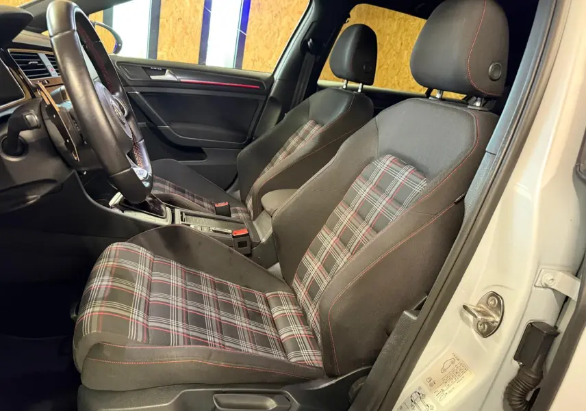 Gros plan sur le volant noir avec surpiqûres rouges et tableau de bord numérique de la Volkswagen Golf GTI Performance gris.