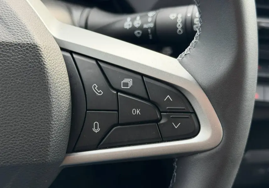 Gros plan sur les commandes multifonctions noires du volant du Dacia Duster 2025, finition Sandstone.