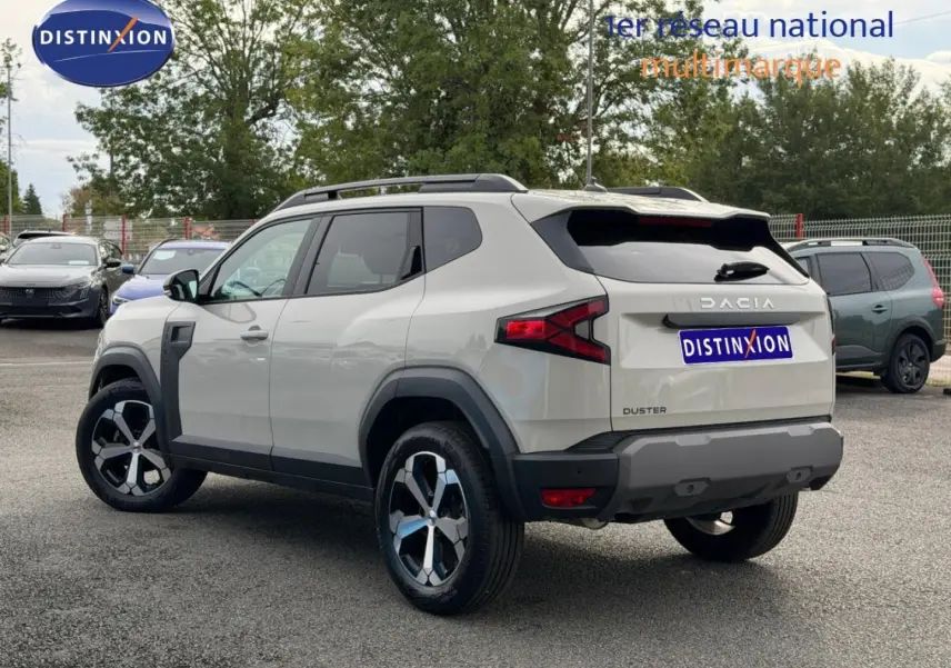 Vue 3/4 arrière droite du Dacia Duster 2025 couleur Sandstone avec jantes alliage et barres de toit noires.