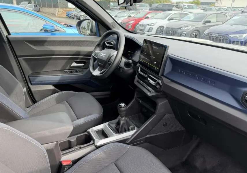 Intérieur du Dacia Duster 2025 vue côté conducteur, planche de bord bleu Sandstone avec écran tactile et boîte manuelle.