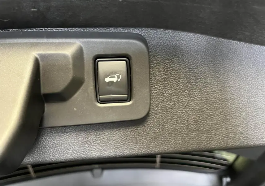 Bouton d'ouverture mains-libres du hayon sur le panneau intérieur noir du coffre du Renault Austral bleu 2023