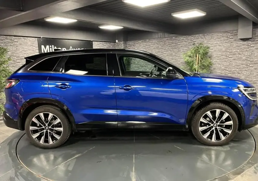 Profil côté gauche du Renault Austral 2023 bleu avec toit noir et jantes alliage noires diamantées dans un showroom.