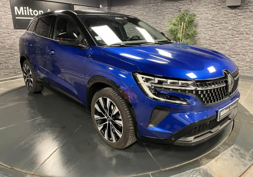 Vue 3/4 avant droite d'un Renault Austral bleu avec calandre à damier chrome sombre et jantes alliage noires diamantées.