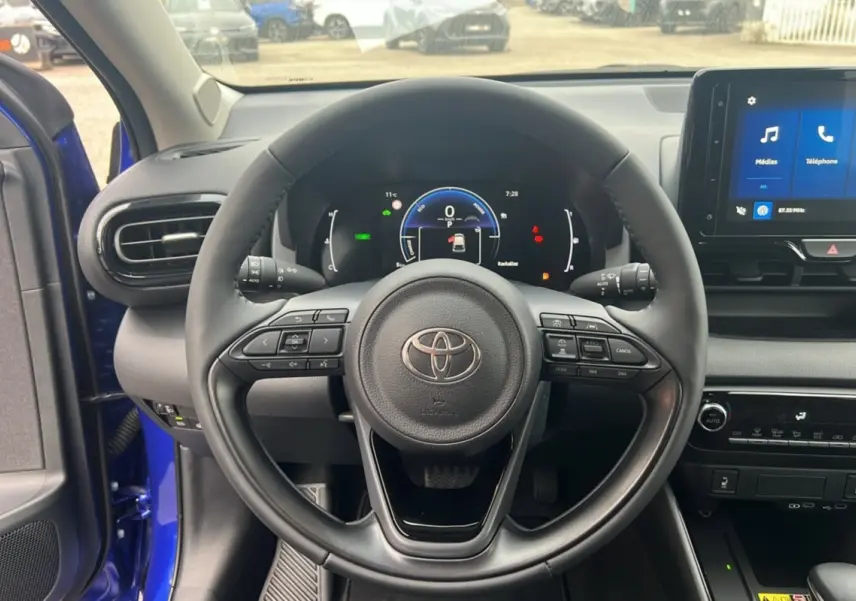 Vue intérieure centrée sur le volant de la Toyota Yaris 2025 bleu genievre avec tableau de bord numérique et écran tactile.