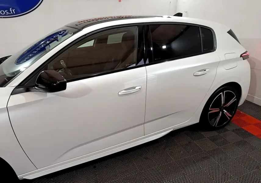 Profil côté gauche d'une Peugeot 308 PHEV 180 E-EAT8 GT blanche, avec vitres teintées et jantes noires stylisées.