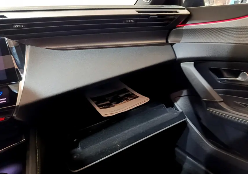 Intérieur côté passager de la Peugeot 308 PHEV 180 E-EAT8 GT 2022, tableau de bord noir avec boîte à gants ouverte.
