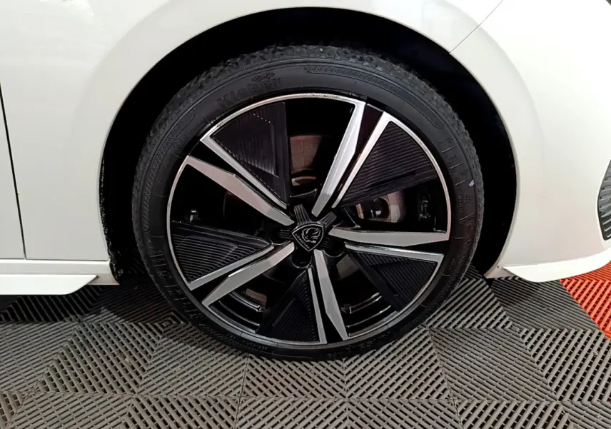 Gros plan sur la roue avant droite noire et argentée d'une Peugeot 308 PHEV 180 E-EAT8 GT blanche.