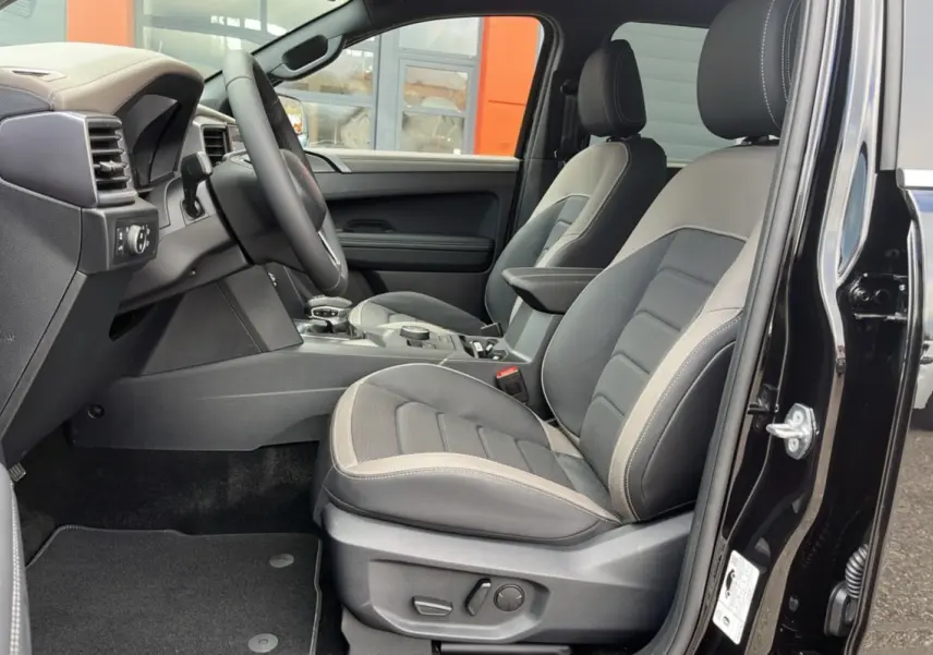 Intérieur côté conducteur du Volkswagen Amarok noir, avec sièges cuir gris et commandes électriques visibles.