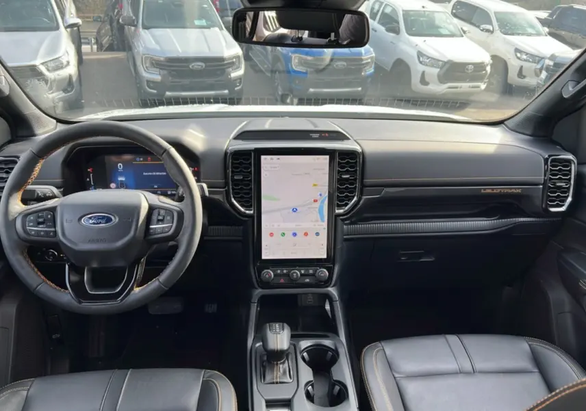 Vue intérieure avant du Ford Ranger Wildtrak 2026, tableau de bord noir avec écran tactile vertical et volant cuir noir.