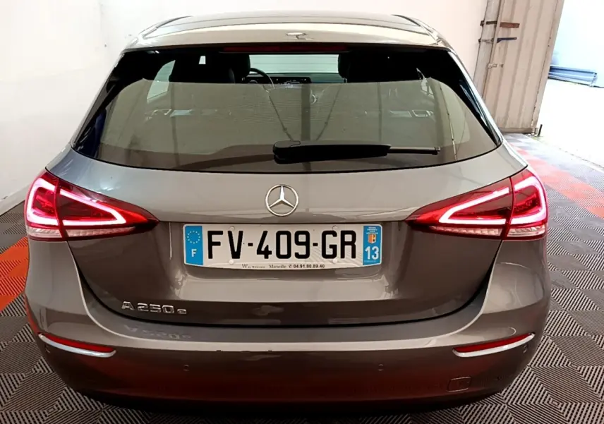 Vue arrière d'une Mercedes Classe A 250 e hybride rechargeable gris métallisé avec feux LED allumés dans un garage.