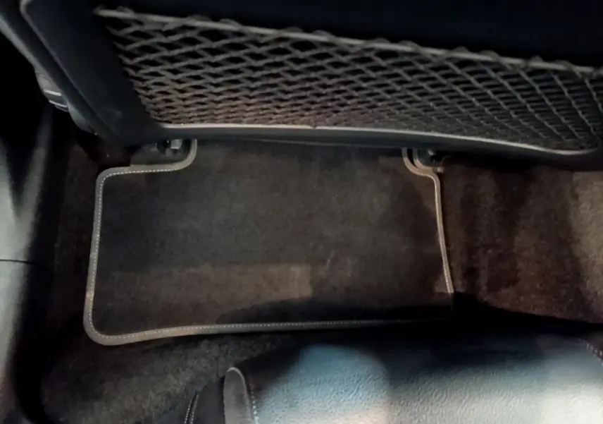 Vue intérieure du plancher arrière avec tapis de sol noir et filet de rangement sous le siège avant d'une Mercedes Classe A hybride.