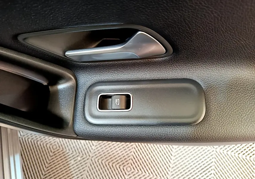 Détail de la poignée intérieure et bouton de lève-vitre électrique côté gauche d'une Mercedes Classe A hybride rechargeable noire.