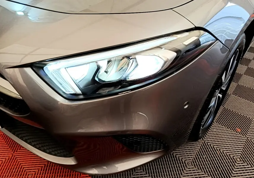 Gros plan sur le phare avant droit d’une Mercedes Classe A 250 e Business Line gris métallisé avec jante alliage visible.