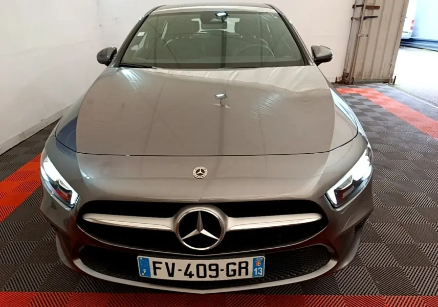 Vue avant d'une Mercedes Classe A grise avec phares allumés, calandre chromée et logo central visible.