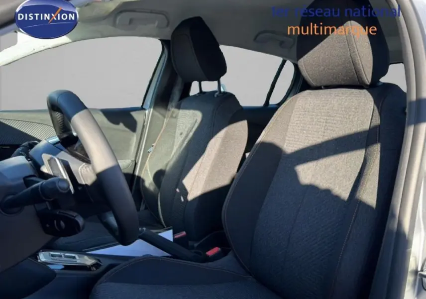 Vue intérieure côté conducteur de la Peugeot 208 gris 2025, mettant en valeur les sièges en tissu et le volant cuir.