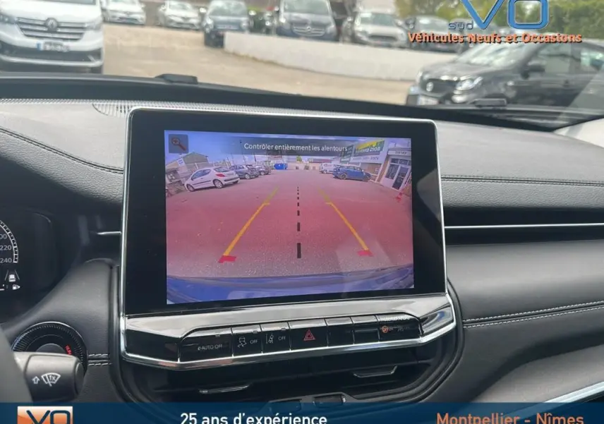 Vue intérieure du tableau de bord du Jeep Compass bleu 2023 avec écran tactile affichant la caméra de recul et aides au stationnement.